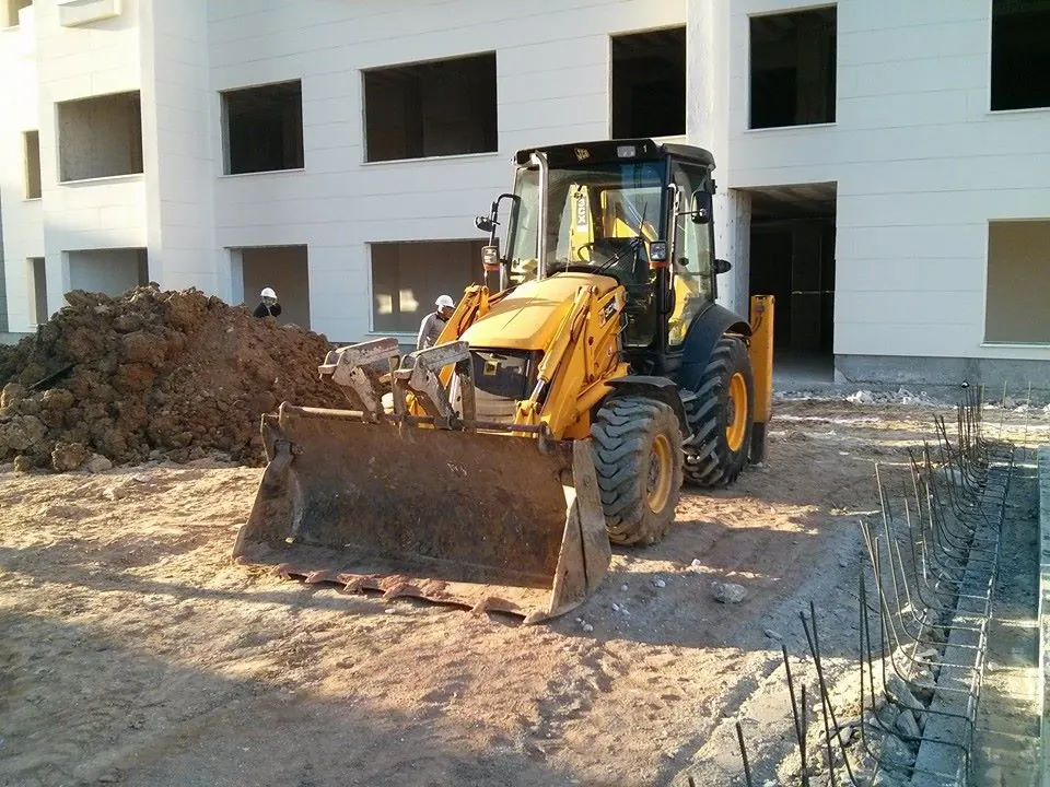 Bina önünde kova ile çalışan sarı kazıcı-yükleyici